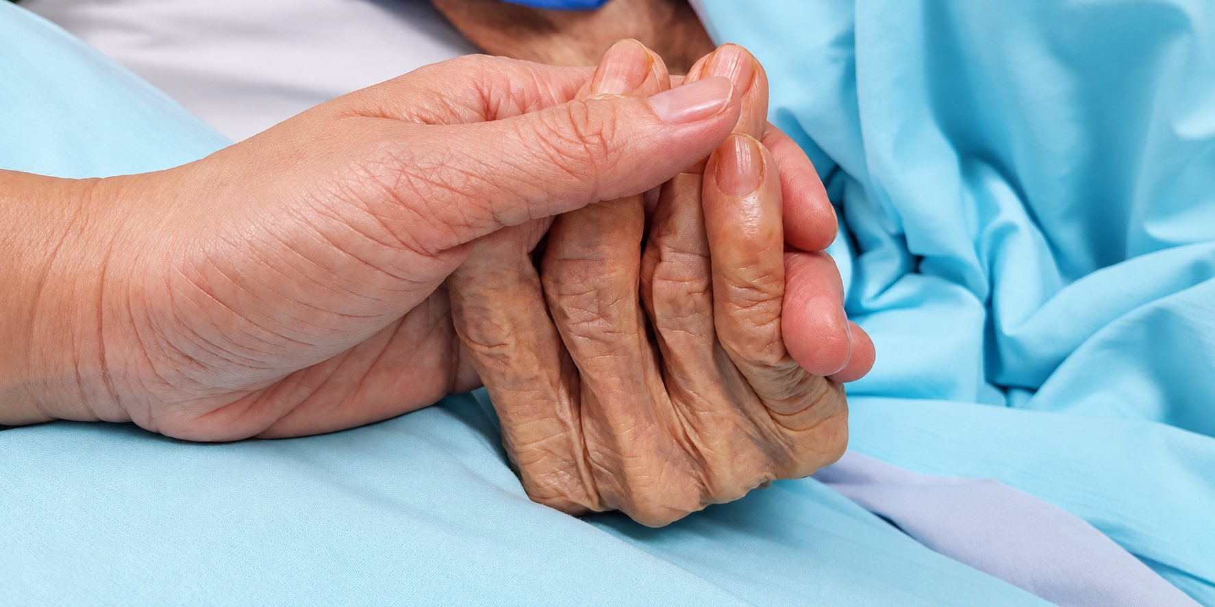 Une main tient celle d’une personne âgée allongée dans un lit.